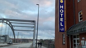 A hotel with a prominent sign, a pedestrian walkway, and a bridge in the background.