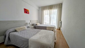 A hotel room with two beds, a nightstand, a lamp, a red sign on the wall, and a large window with curtains. - Apartment,Rincon de Loix, Benidorm, sea views, s.pool, pk, air conditioning,wifi (Benidorm)