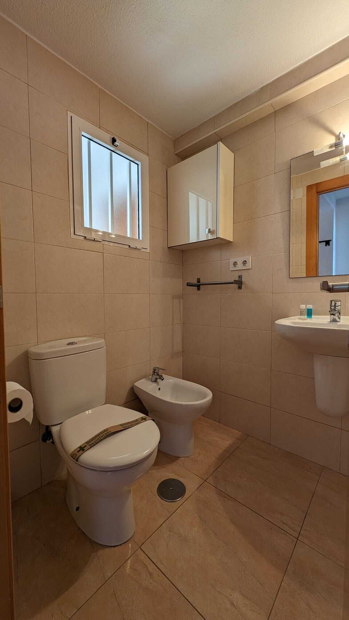 Une salle de bain avec deux toilettes, un bidet, un lavabo, un miroir et une fenêtre.