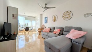 A modern living room with a grey sofa, a flat-screen TV, and a dining area with a table and chairs. - Apartment,Rincon de Loix, Benidorm, sea views, s.pool, pk, air conditioning,wifi (Benidorm)