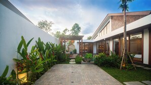Un patio con sendero adoquinado, plantas en macetas y un pérgola.