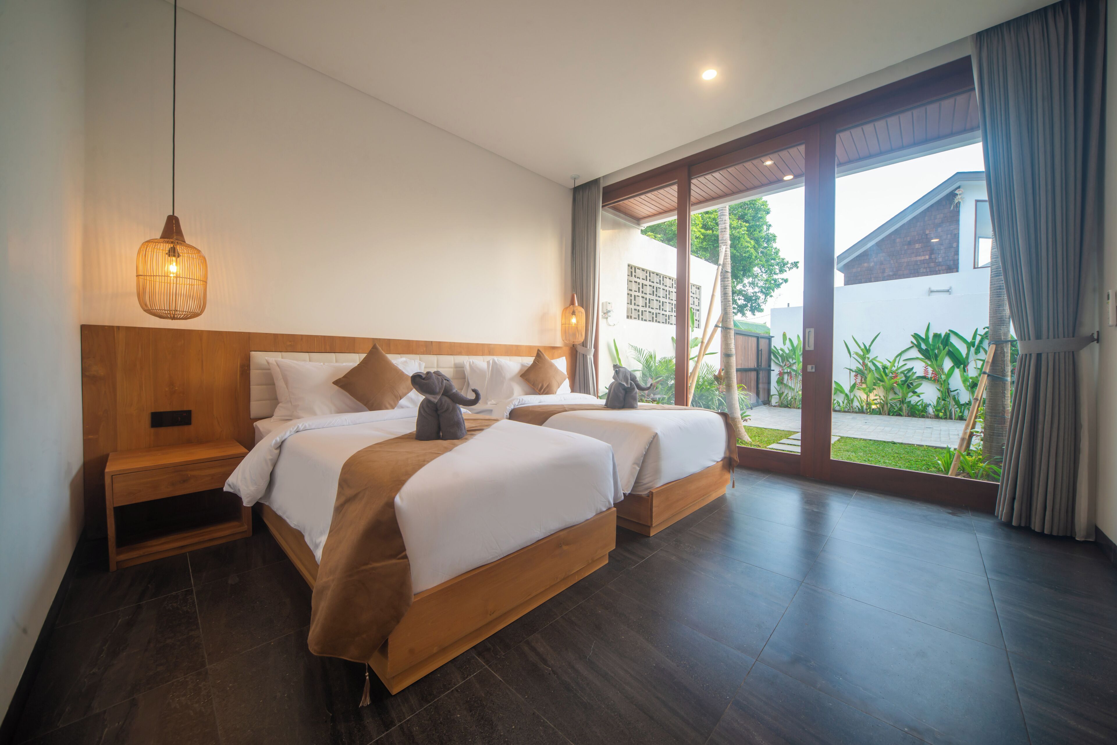 Habitación de hotel con dos camas, cabeceros de madera y un amplio ventanal corredero que da a un jardín.