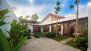 Una casa moderna con un patio cubierto, piscina y abundante vegetación.