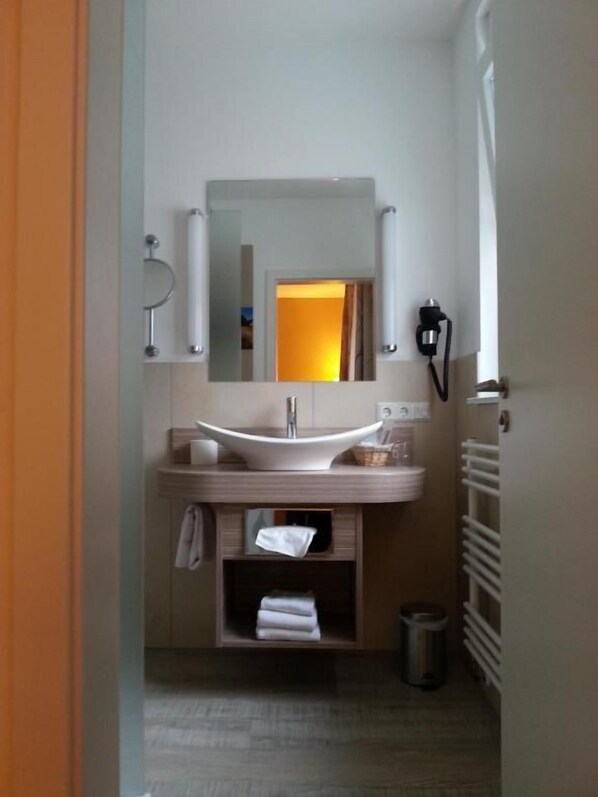 Une salle de bain équipée d’un lavabo, d’un miroir, d’un porte-serviettes et d’une petite poubelle.