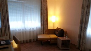 Ett hotellrum med en soffa, ett litet bord, en lampa och ett skrivbord med en stol.