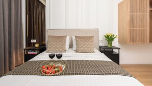 A neatly made bed with a patterned bedspread, two bedside tables with books and a vase of flowers, and a large window with curtains. - Lumina luxury 4-rooms apart with parking (Łódź)