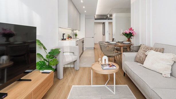 A modern living room with a sofa, coffee table, and TV stand. There is a dining area with a table and chairs. - Lumina luxury 4-rooms apart with parking (Łódź)