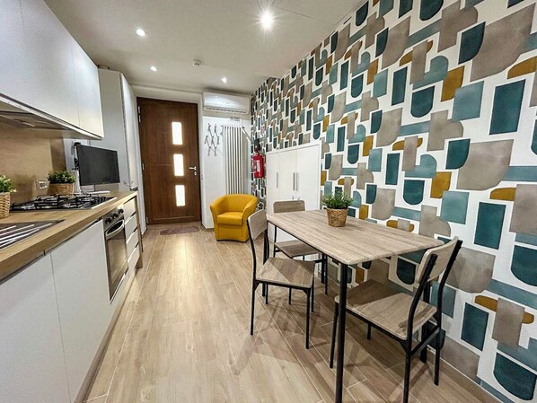 Una cocina moderna con comedor, que incluye una mesa y sillas de madera, un sillón amarillo y un papel tapiz decorado.