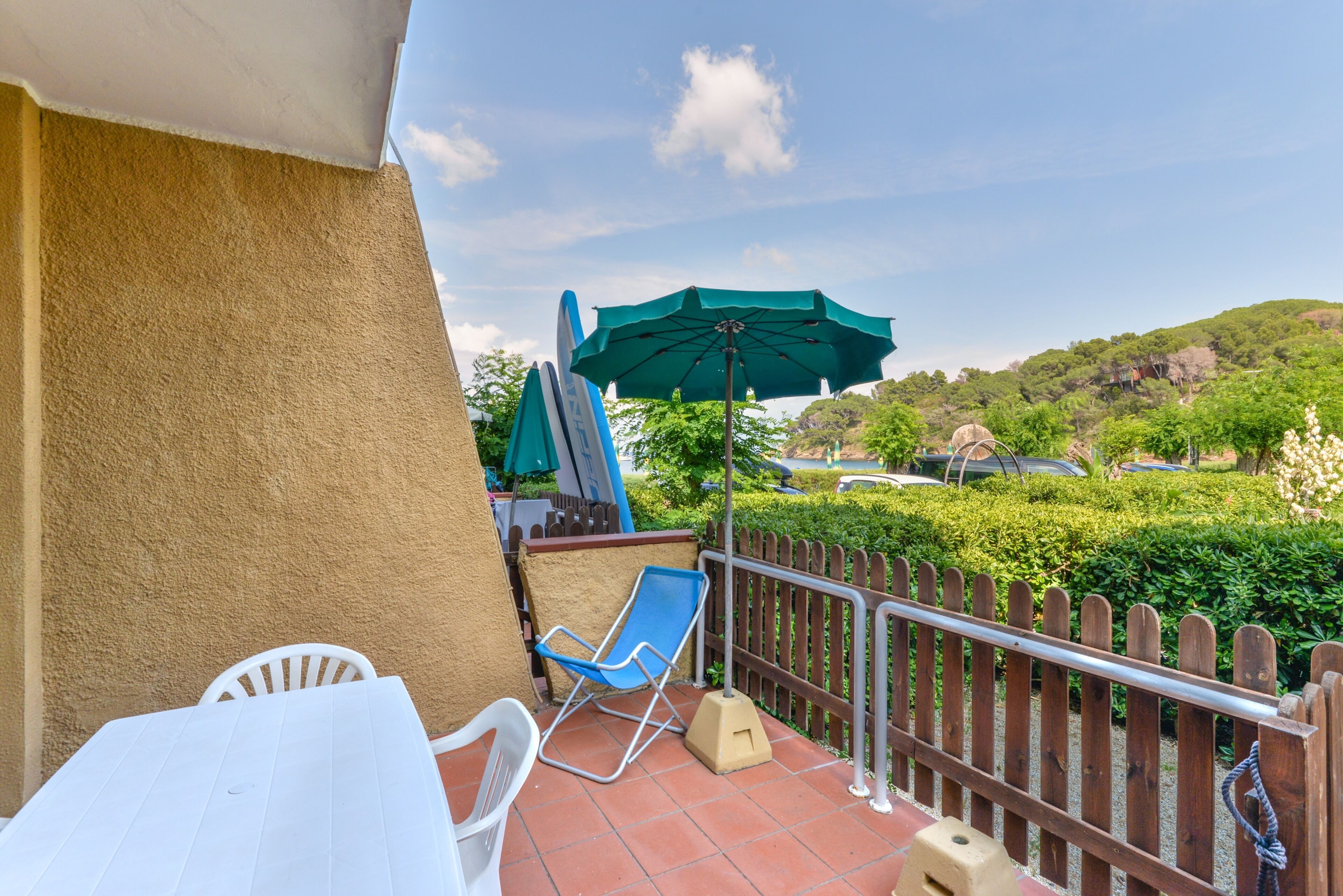 A balcony with a white table and chairs, a blue lounge chair, and a green umbrella.