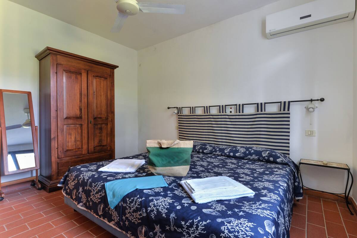 A bedroom with a large bed, a wooden wardrobe, a mirror, and a small table.
