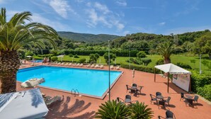 A swimming pool with lounge chairs and umbrellas, surrounded by lush greenery and hills in the background. - Residence in Capoliveri just 200 mt from the beach  (Capoliveri)