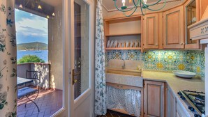 A kitchen with wooden cabinets, a tiled backsplash, and a window overlooking a balcony. - Residence in Capoliveri just 200 mt from the beach  (Capoliveri)