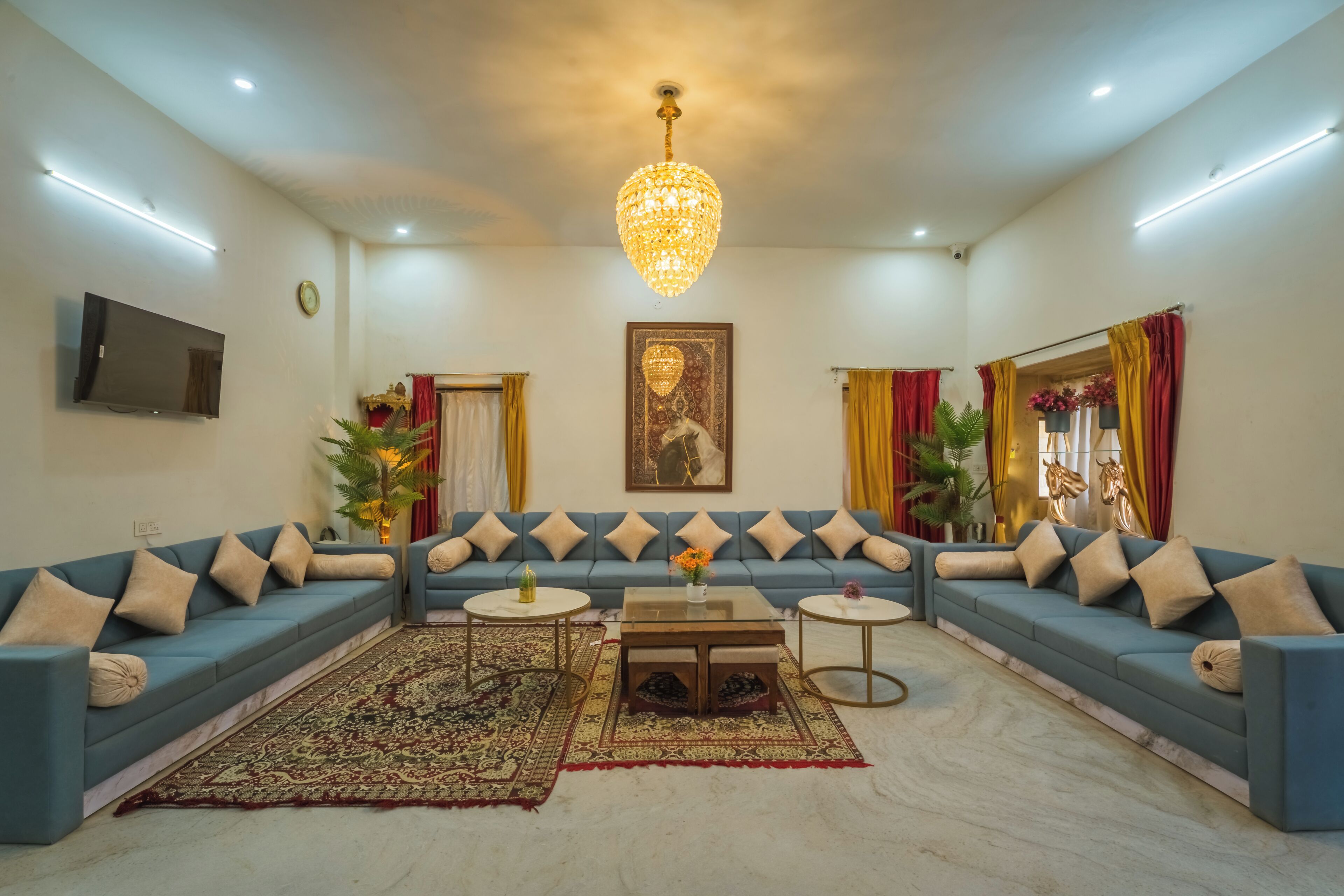 A living room with a blue sofa set, a chandelier, a flat-screen TV, and a large painting on the wall.