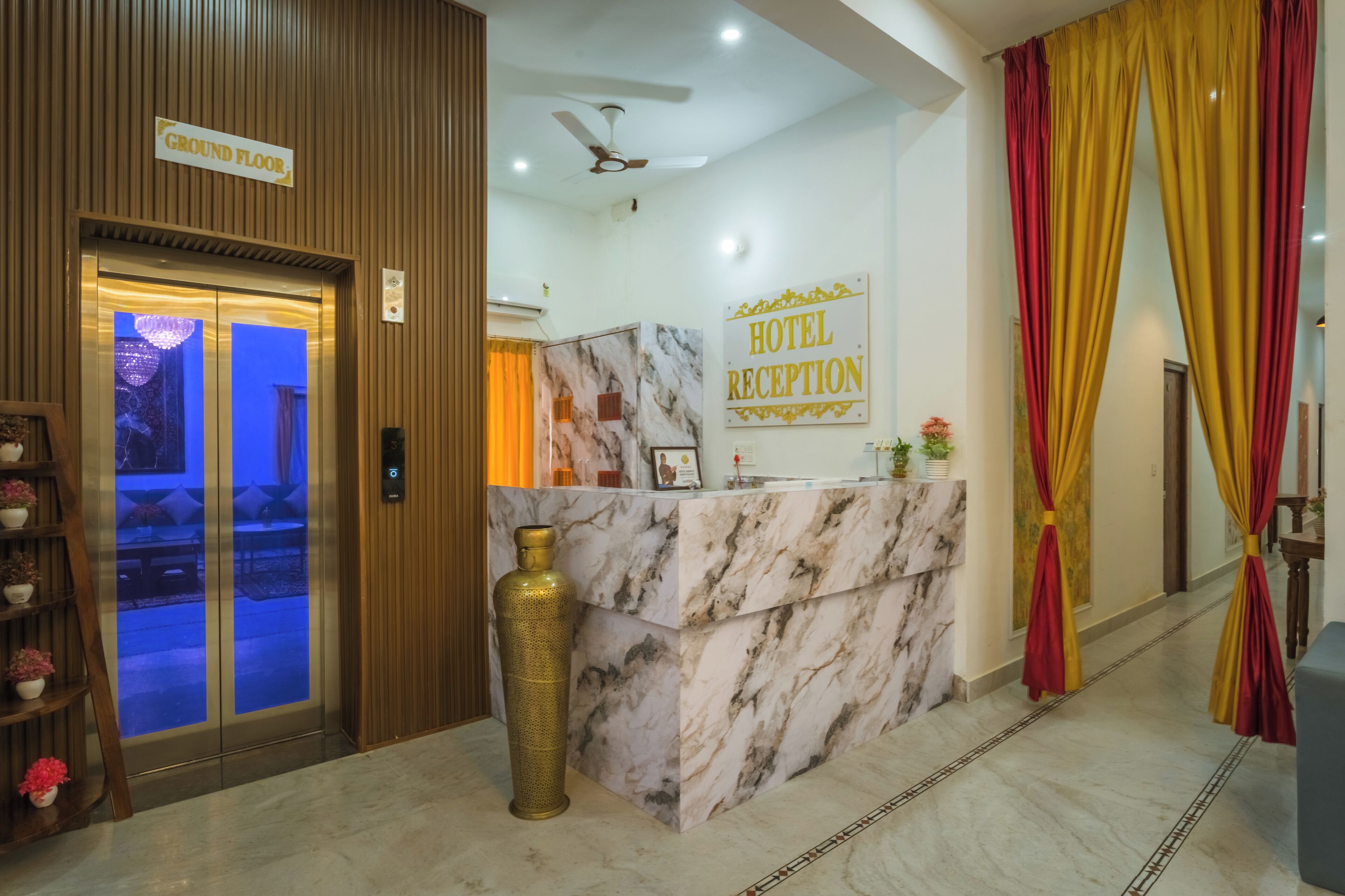A hotel reception area with a marble reception desk, a sign indicating the ground floor, and a large vase.