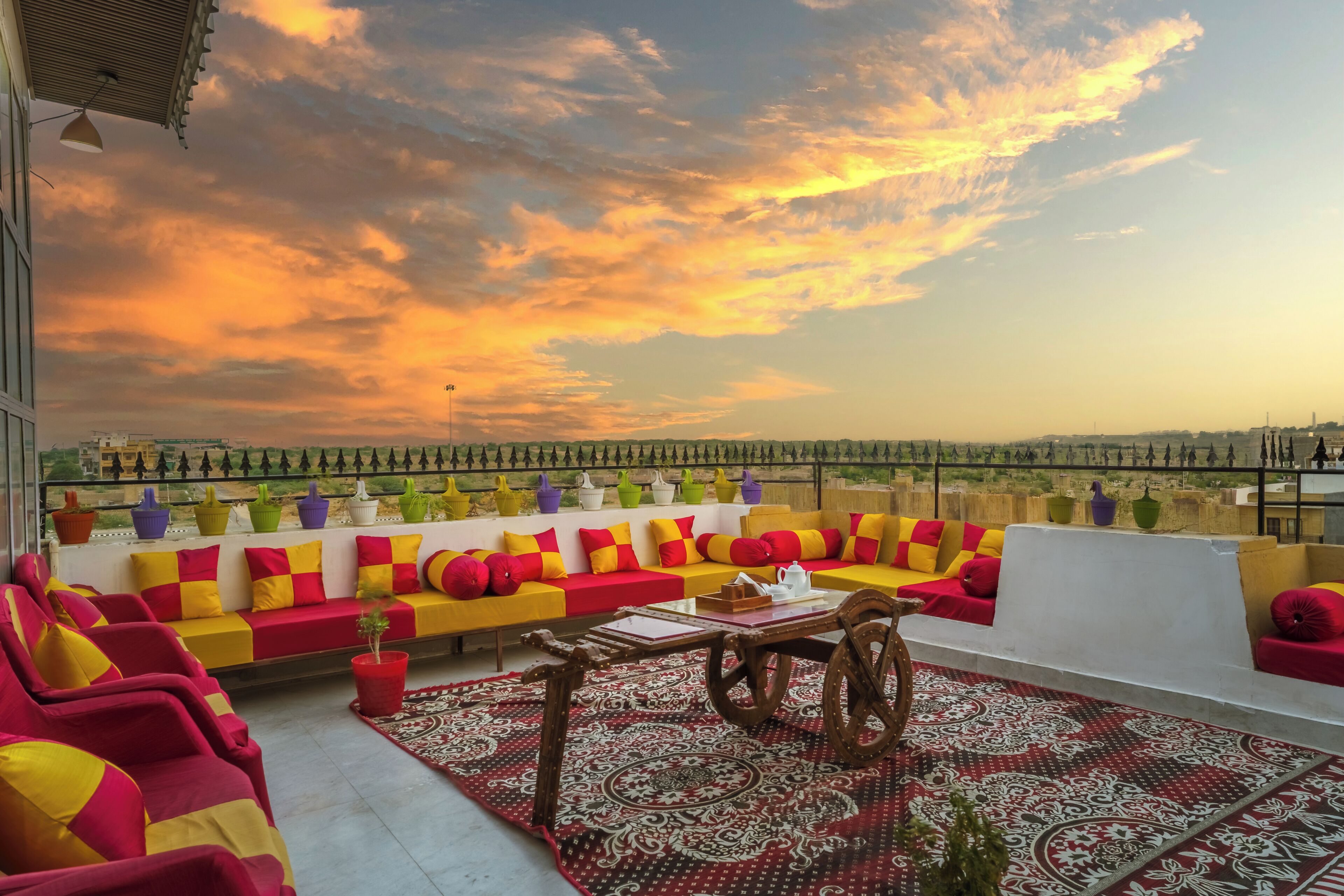 Una terraza en la azotea con un conjunto de sofás, una mesa con tetera y vistas del paisaje urbano al atardecer.