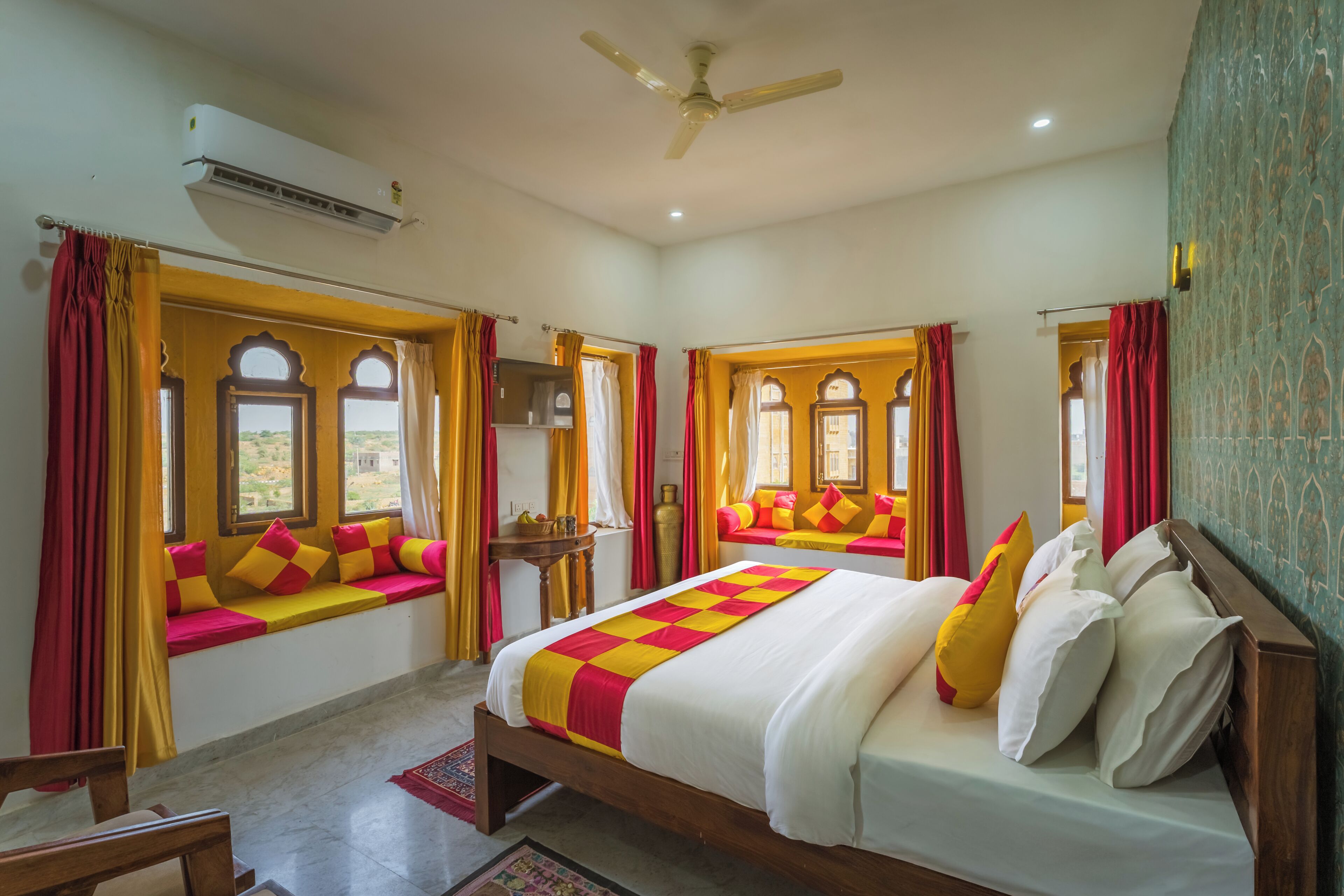 Habitación de hotel con cama, asiento junto a la ventana, ventilador de techo y aire acondicionado de pared.