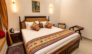 A neatly made bed with a colorful blanket, a wooden headboard, and a nightstand with a kettle and glass.