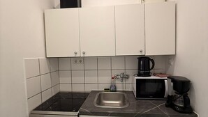 Pieni, käytännöllinen keittiö, jossa on valkoiset kaapit, mikroaaltouuni, kahvinkeitin ja liesi.
