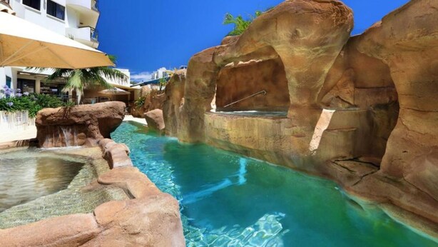 A pool area with clear water, rock formations, and a lounge area with umbrellas. - 62 at the Caribbean Resort (mooloolaba)