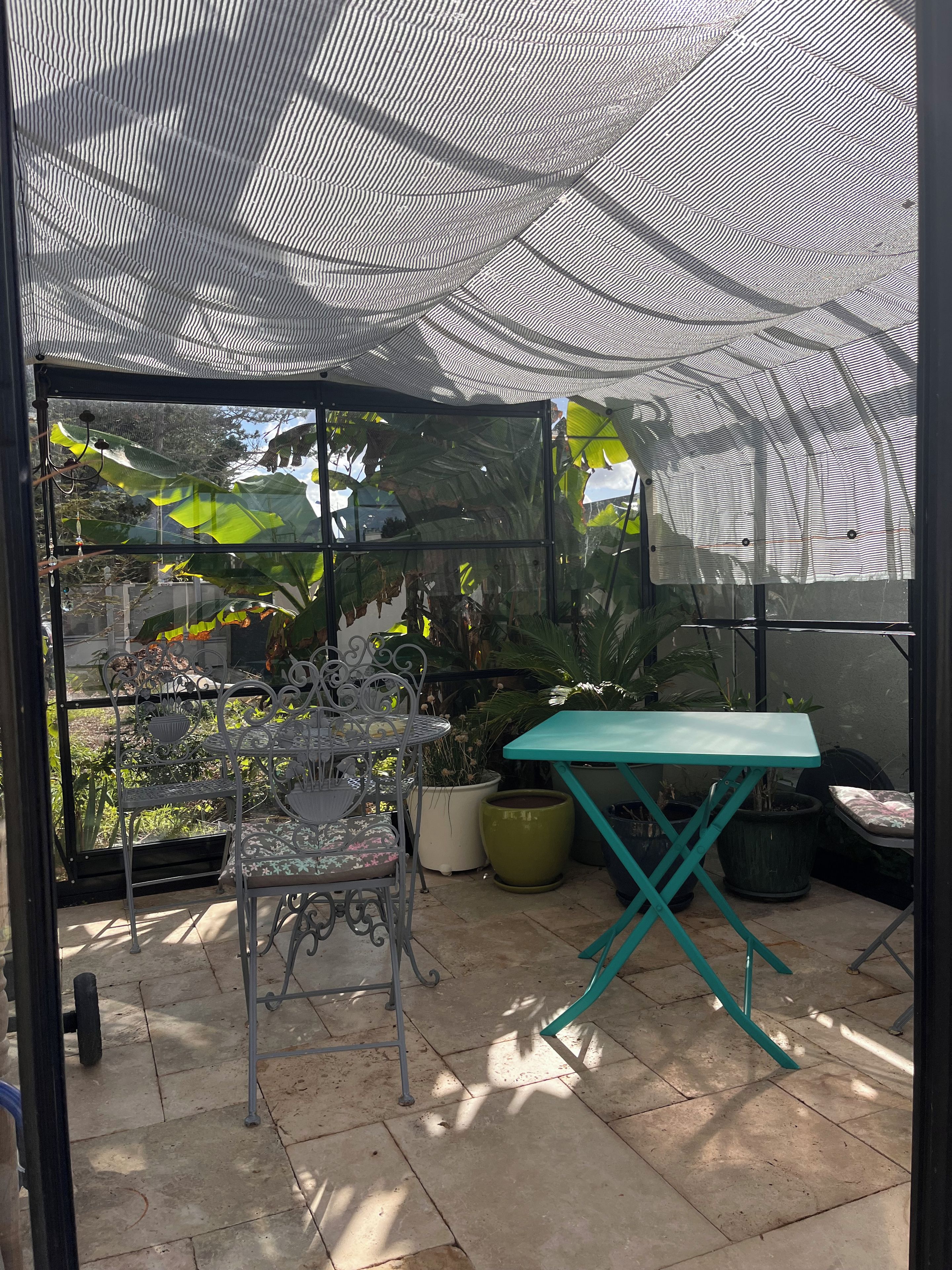 Ein überdachter Patio-Bereich mit einem Metalltisch und -stühlen, Topfpflanzen und Blick ins Grüne.