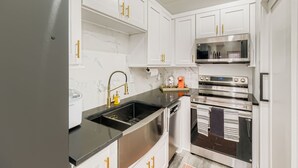 A compact kitchen with white cabinets, a black countertop, and stainless steel appliances including a refrigerator, oven, and microwave. - Tiny Home Atlanta Retreat (Union City)