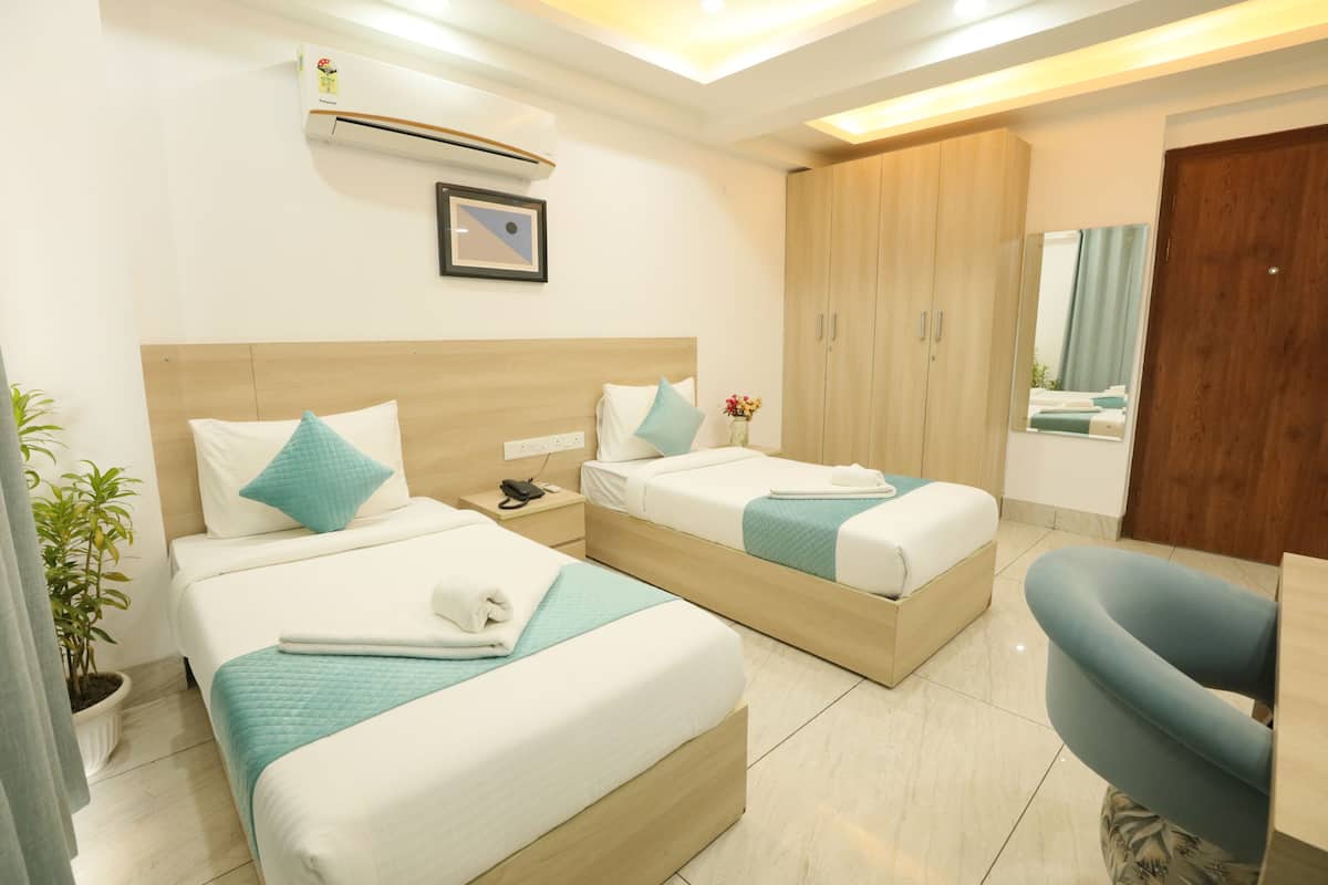 A hotel room with two beds, a wooden wardrobe, a mirror, and a potted plant.