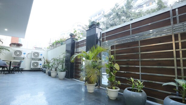 A modern outdoor area with potted plants, air conditioning units, and a wooden fence. - CORPORATE STAYS - GOLF COURSE ROAD (Gurugram)