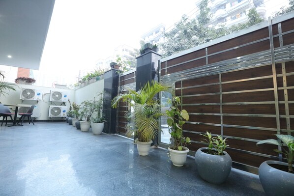A modern outdoor area with potted plants, air conditioning units, and a wooden fence. - CORPORATE STAYS - GOLF COURSE ROAD (Gurugram)