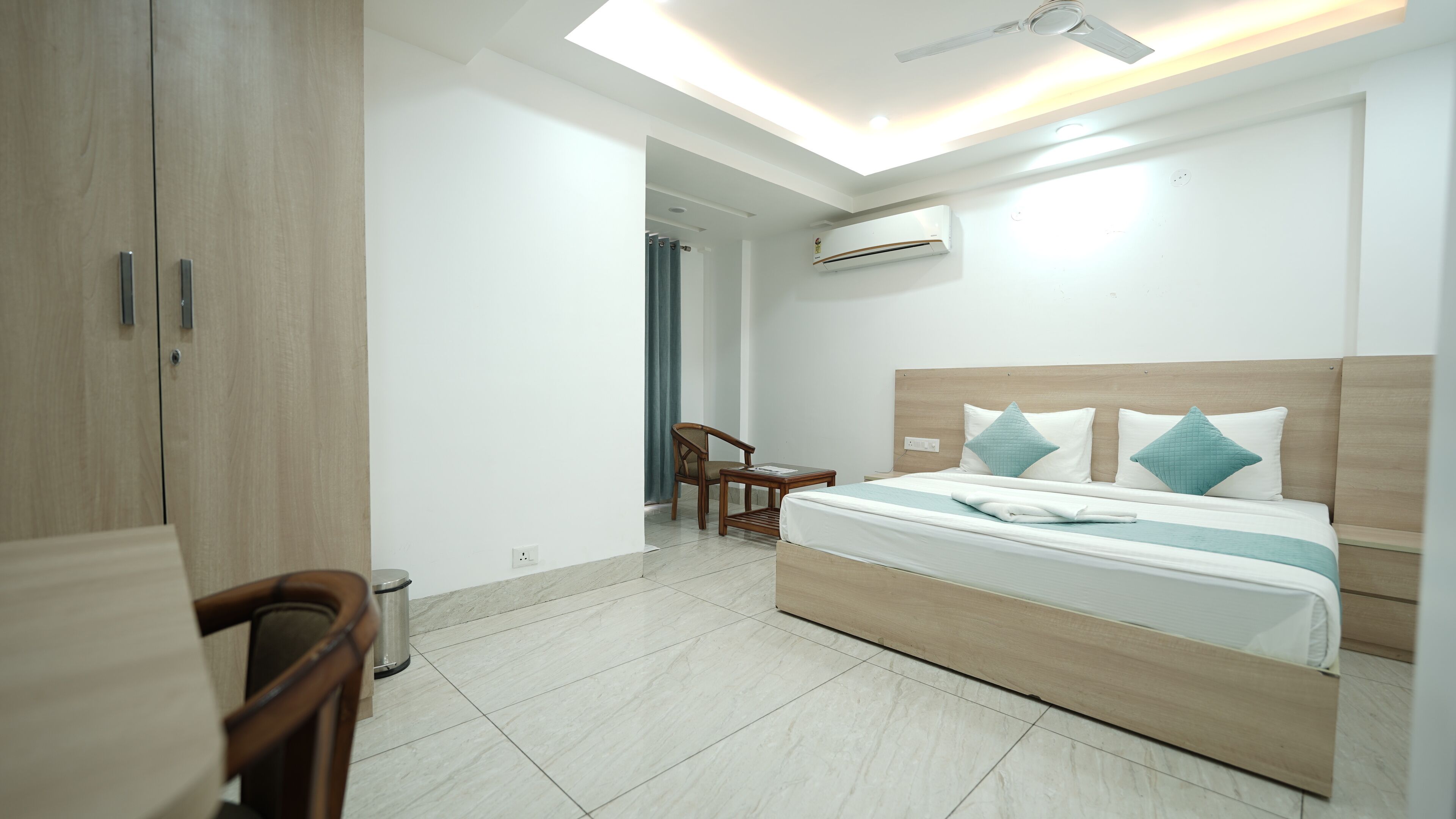 Un dormitorio moderno con una cama de madera, una silla, una mesita y un ventilador de techo.