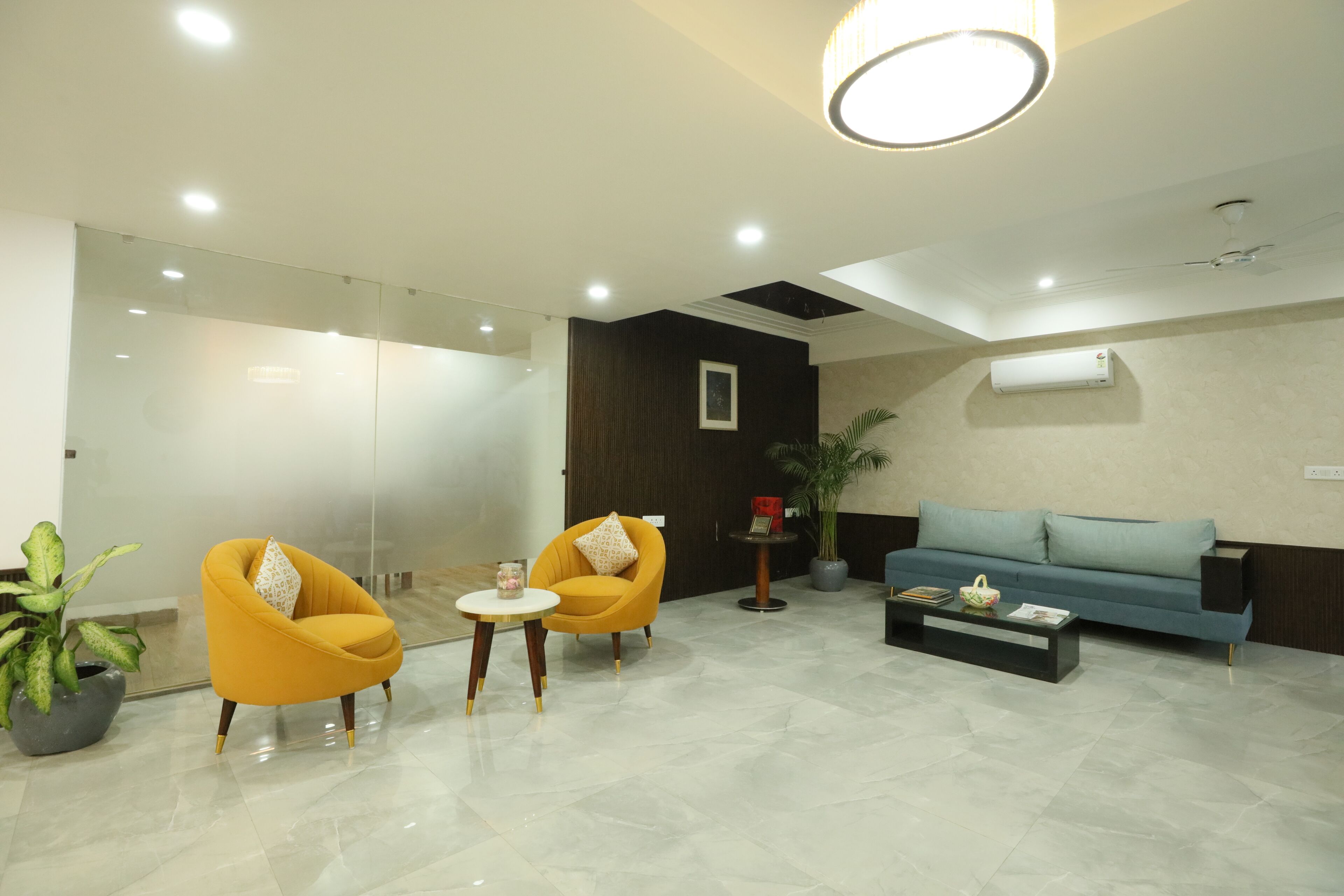 Eine moderne Lobby mit zwei gelben Sessel, einem blauen Sofa, einem Couchtisch und einer Topfpflanze.