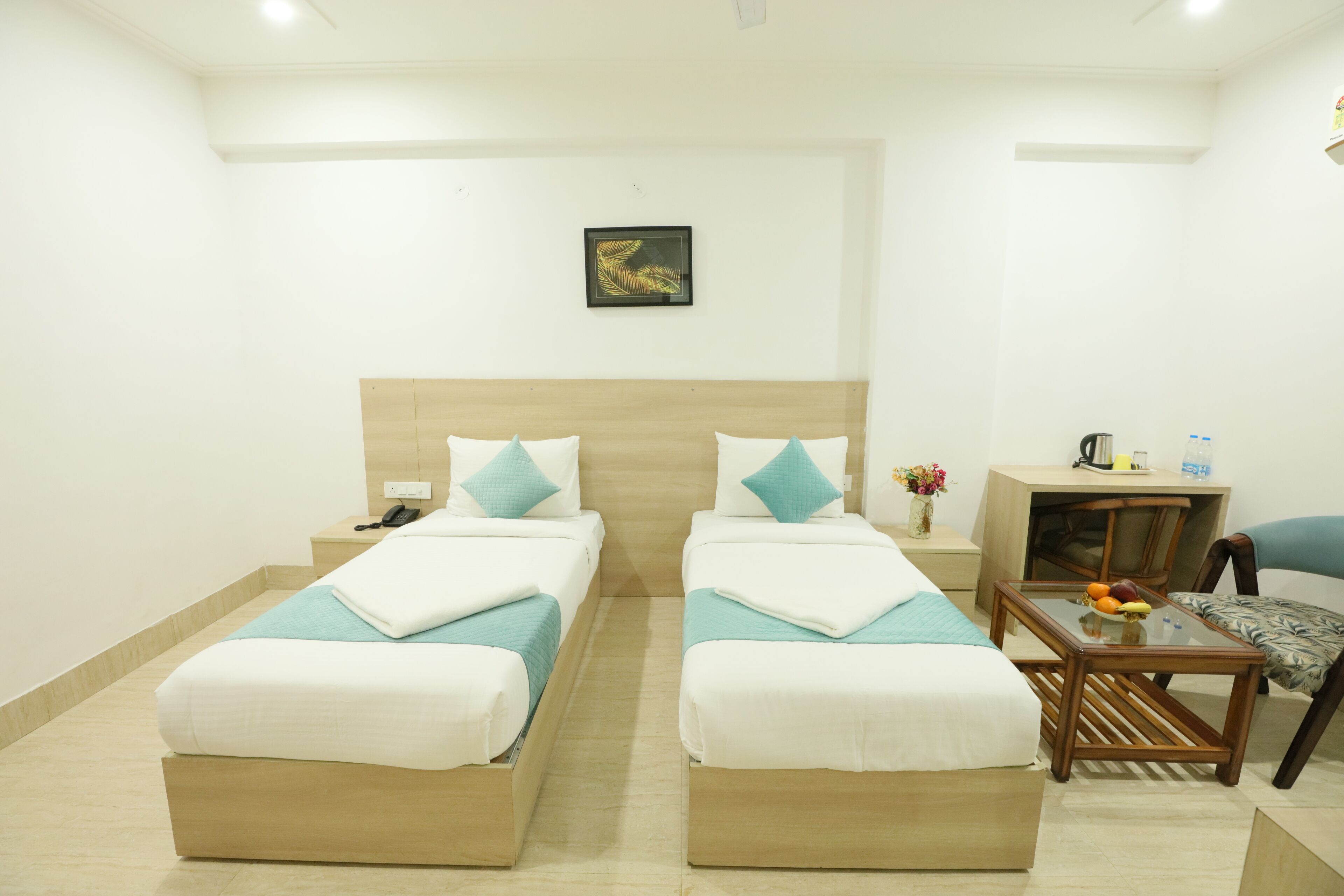 A hotel room with two beds, a small table with fruit, a chair, and a desk with a lamp and a vase of flowers.
