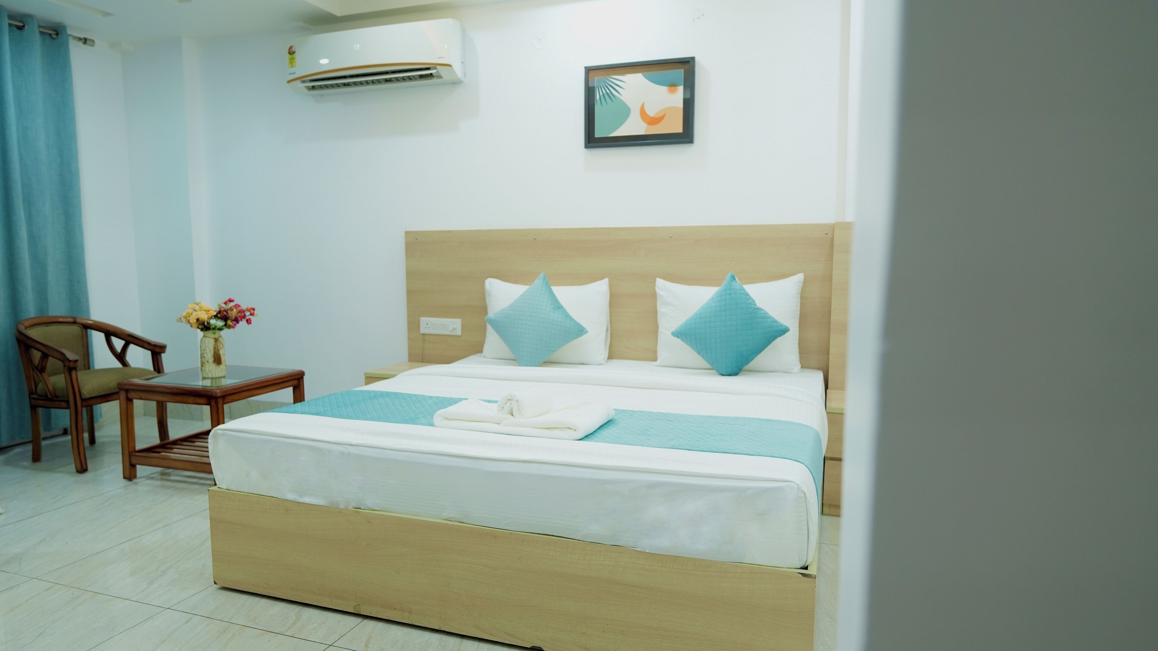 Une chambre d’hôtel comprenant un lit, une tête de lit en bois, une table de chevet, une chaise et un climatiseur fixé au mur.