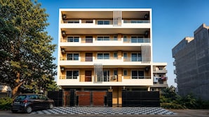 Un edificio de varios pisos con balcones, un acceso con portón y un automóvil estacionado en la parte delantera.