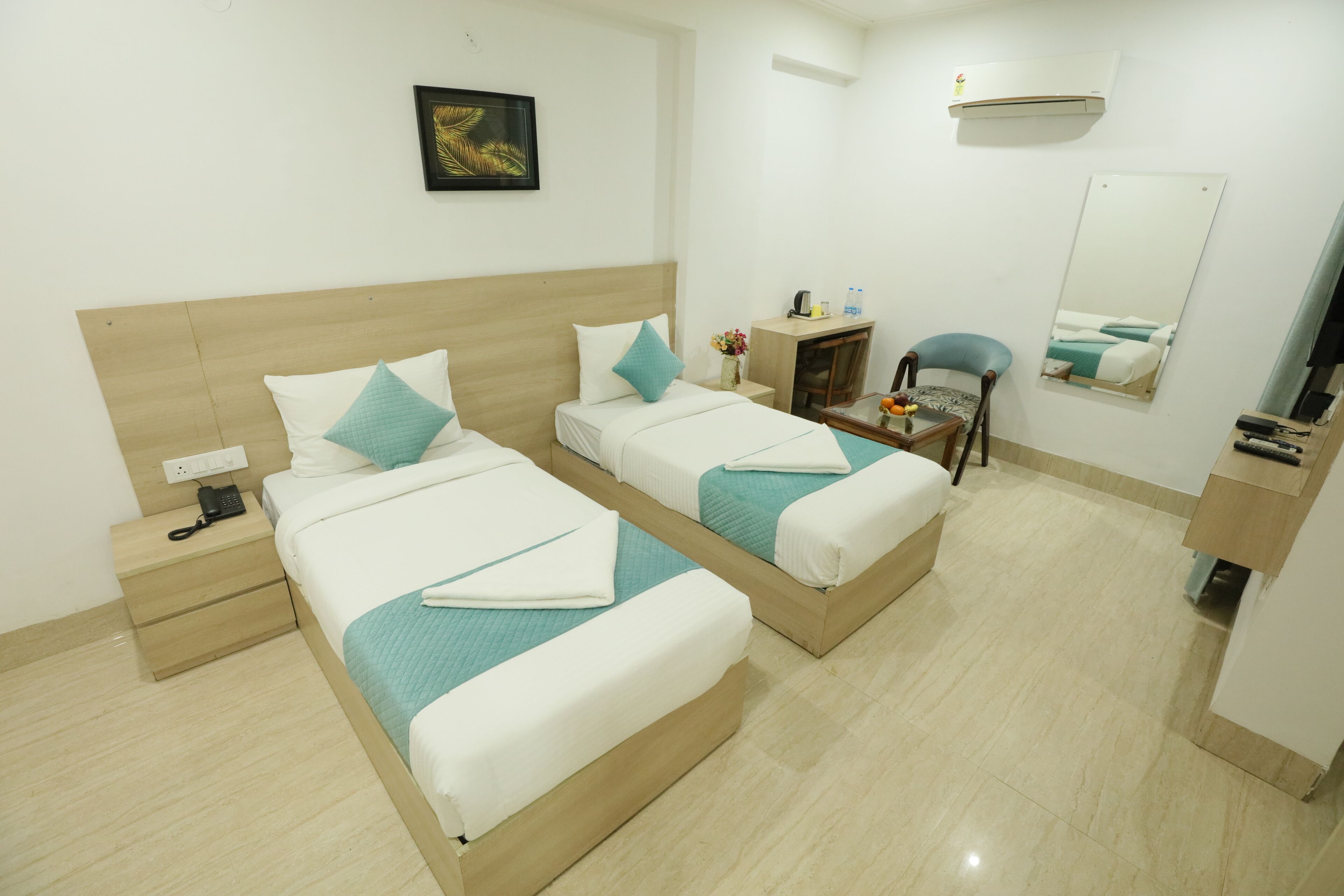 Habitación de hotel con dos camas individuales, una mesita de noche con teléfono, un escritorio pequeño con silla, un espejo y un equipo de aire acondicionado.