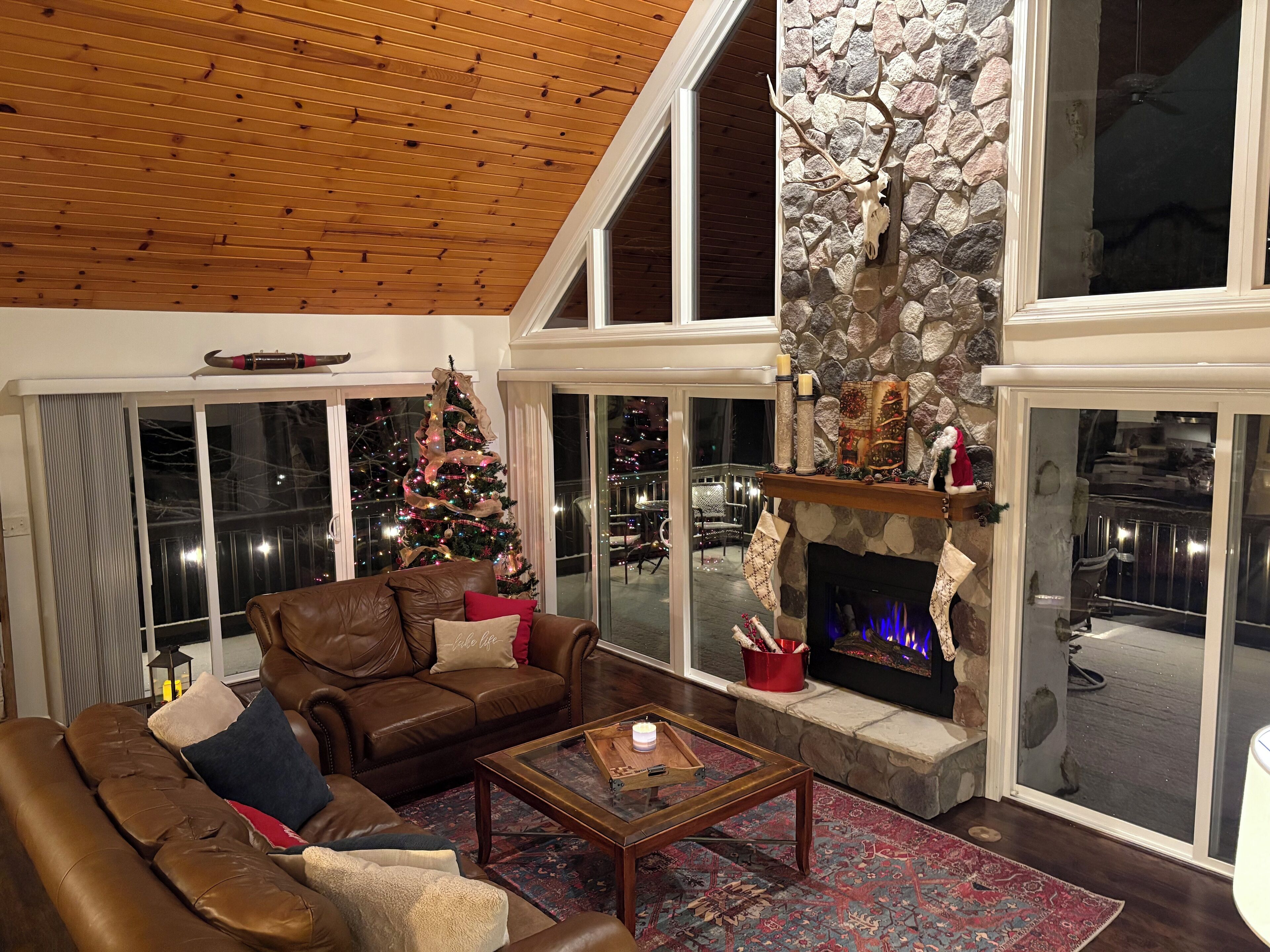 Un salon chaleureux avec un canapé en cuir, une cheminée, un sapin de Noël et un mur en pierre.