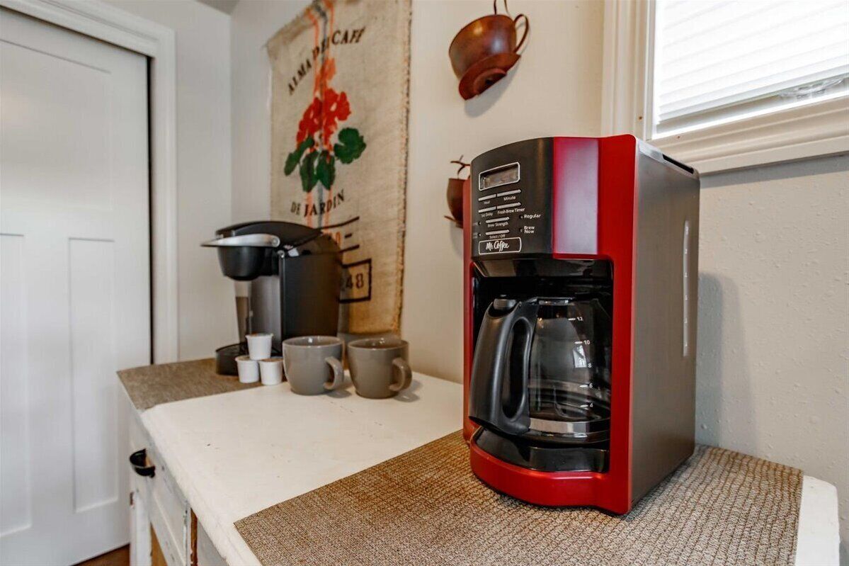 A kitchen with a red coffee maker, a black coffee pot, and several coffee cups on the counter.