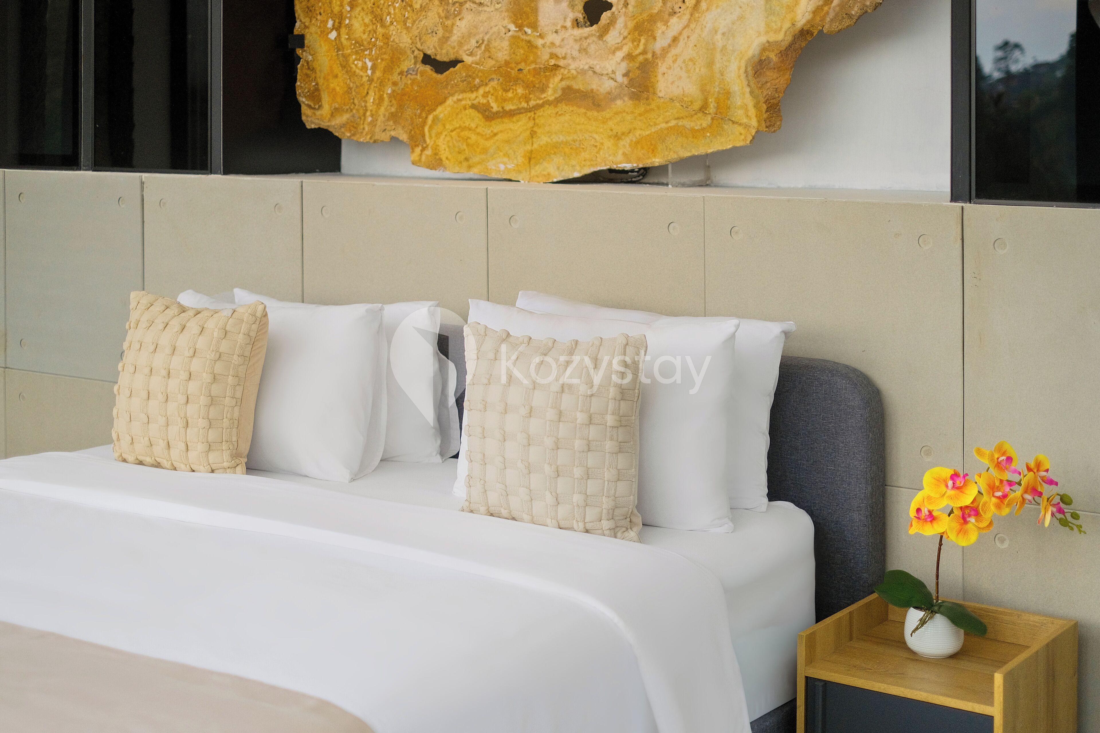 A modern bedroom with a large bed, white bedding, and a wooden nightstand with a vase of flowers.