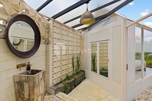 Un baño moderno con un lavabo de piedra, un espejo redondo, una lámpara colgante decorativa y una puerta de cristal que da a un balcón.