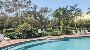 Una piscina con lettini e vegetazione tropicale.