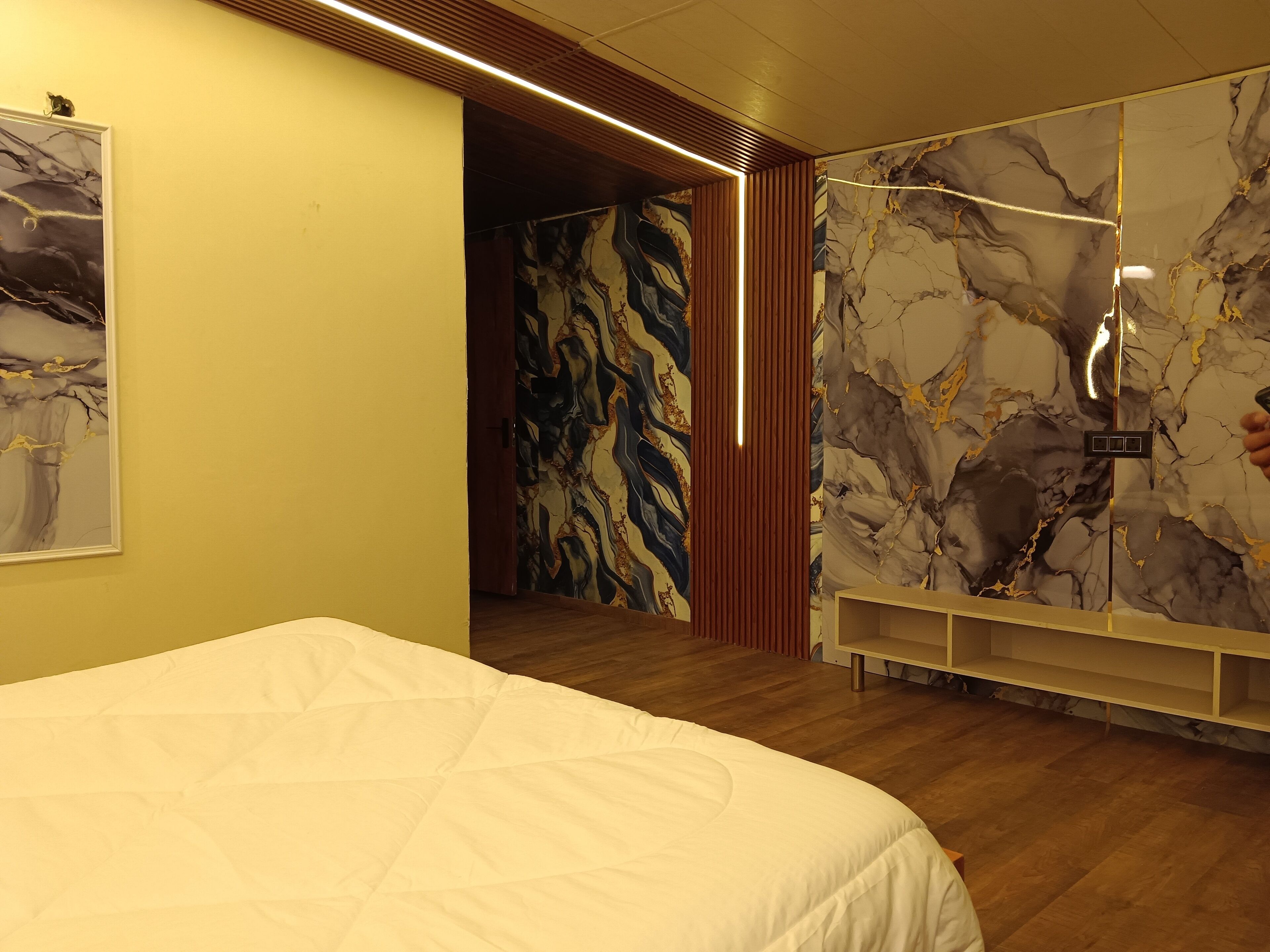 Una habitación de hotel moderna con una cama grande, un muro con diseño de mármol y un techo de madera.