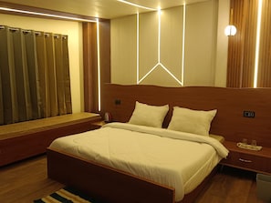 Un dormitorio moderno con cabecera de madera, una cama grande con ropa blanca, una mesita de noche con lámpara y una ventana con cortinas.