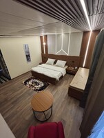 Una habitación de hotel moderna con una cama de madera, una mesita de noche, una pequeña mesa redonda y una silla roja.