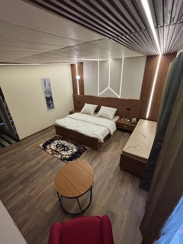 Una habitación de hotel moderna con una cama de madera, una mesita de noche, una pequeña mesa redonda y una silla roja.