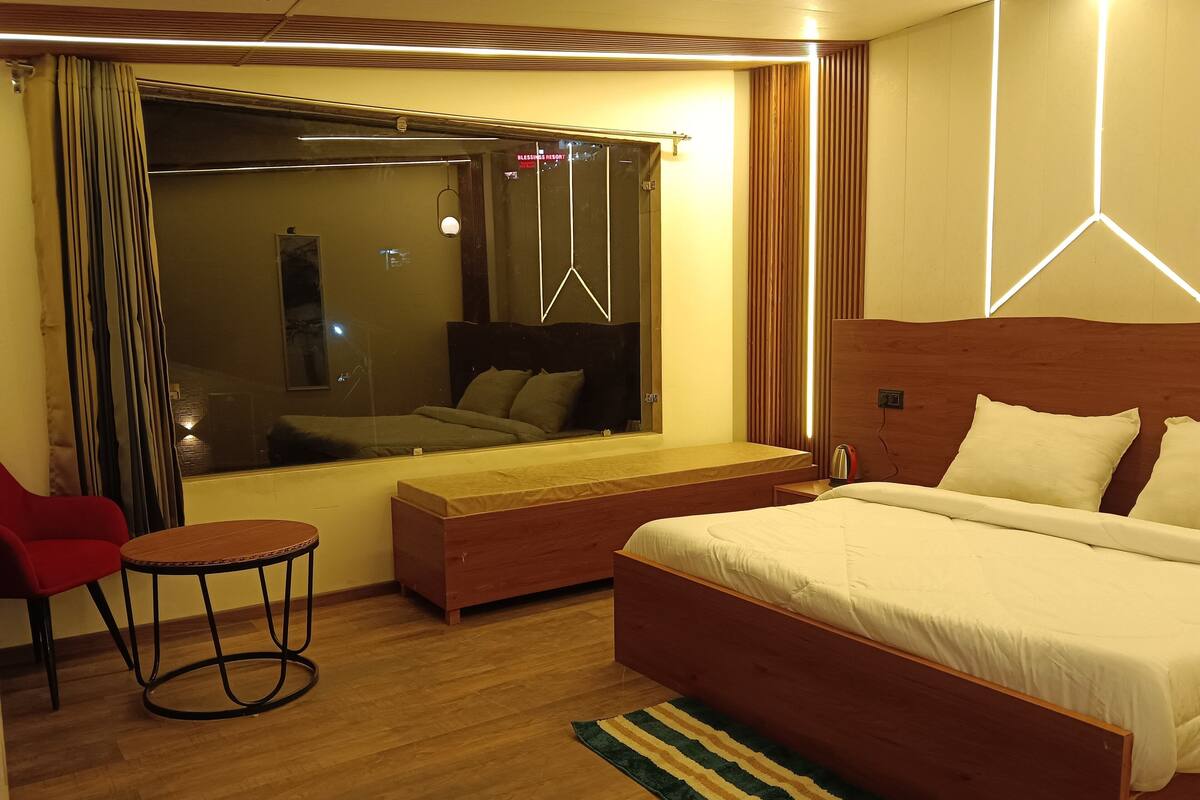 A modern hotel room with a large bed, a small seating area, a window with curtains, and a wooden floor.