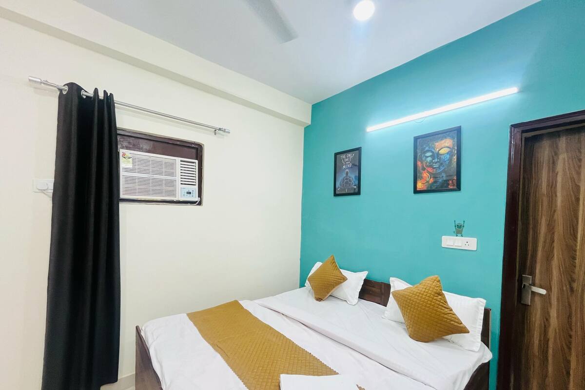 A bedroom with a bed, a window with an air conditioner, a door, and two wall-mounted pictures.