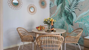 Un coin repas avec des chaises en osier, une table ronde et un mur orné de motifs de feuilles tropicales.