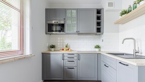 Une cuisine avec des meubles gris, un four en acier inoxydable, un dosseret de carrelage blanc, un plan de travail en bois et un évier encastré.