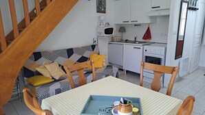 A compact living space with a sofa, dining table, chairs, a kitchen area, and a staircase. - Charming Cottage - Near Beach and Shops (Fort-Mahon-Plage)