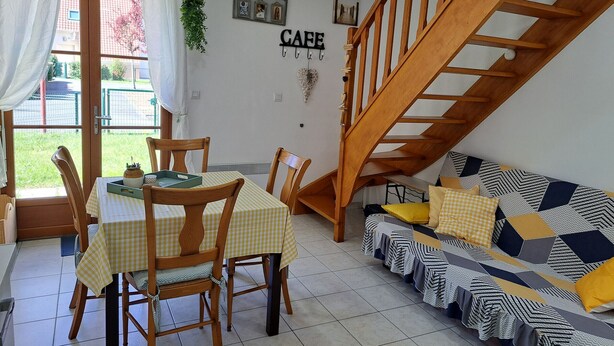 A dining area with a table and chairs, a staircase, and a sofa with patterned cushions. - Charming Cottage - Near Beach and Shops (Fort-Mahon-Plage)