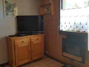 A room with a wooden cabinet, a television, and a window with a view of trees.
